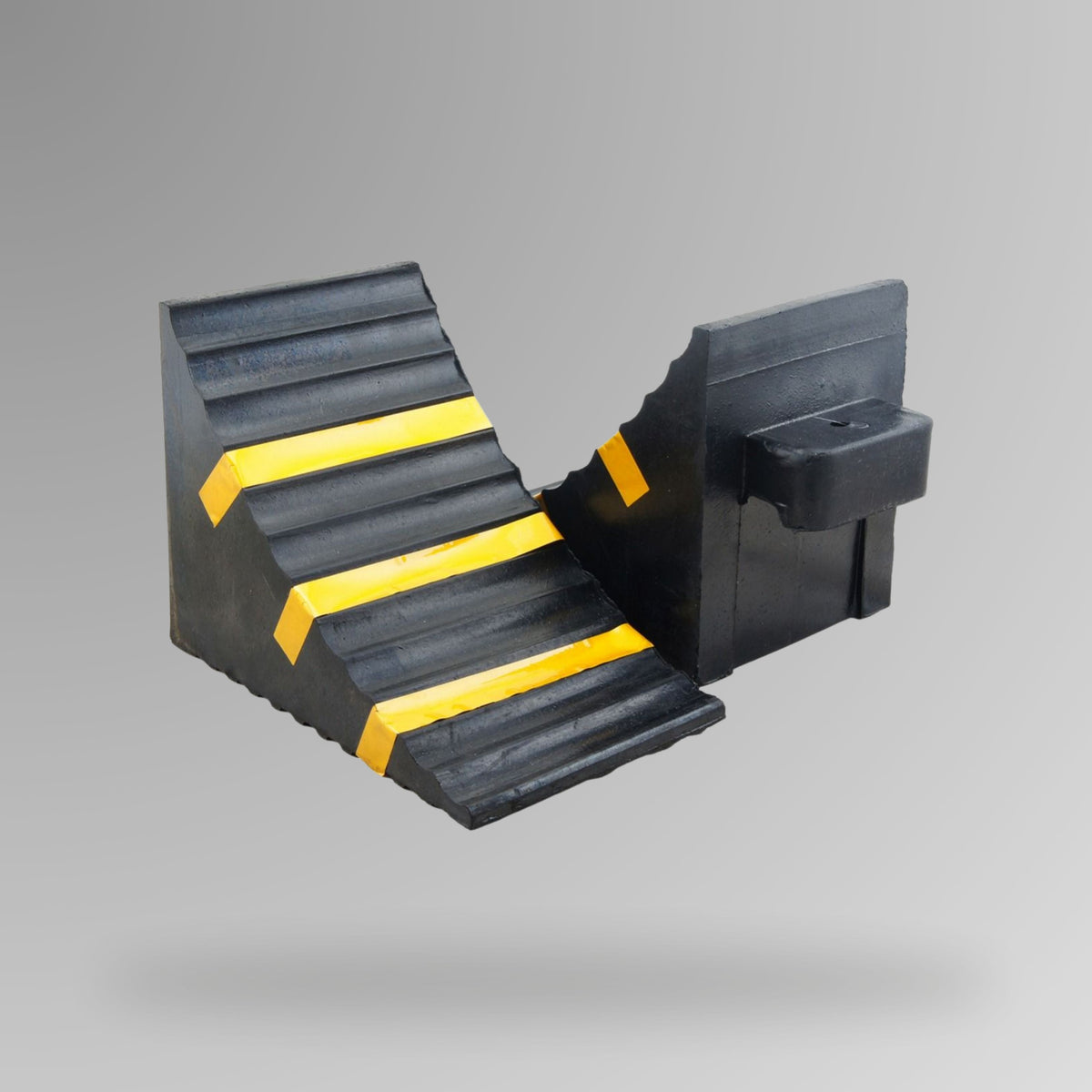 Black rubberised wheel chock shown upright, displaying built-in handle, moulded rope connection point and three contrast yellow tape strips. BVS 001. Brute Safety Products.